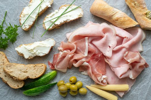 Cold appetizer. Cold cuts. Different snacks on a white crumpled paper, ham, bread, vegetables, from above.