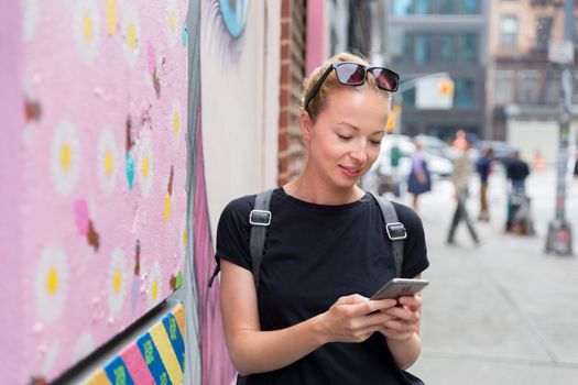 Closeup of female hipster with smart phone. Woman using smartphones against colorful graffiti wall in East Village, New York city, USA.