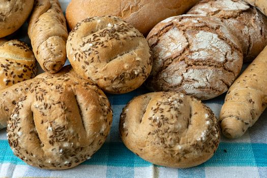 Heap of various bread rolls sprinkled with salt, caraway and sesame. Fresh rustic bread from leavened dough. Assortment of freshly of bakery products