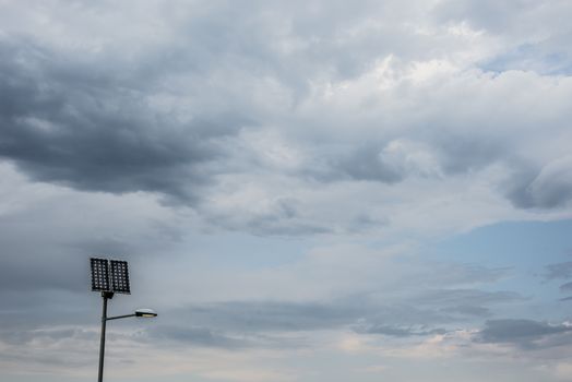 Solar panel on street lamp post with light on and cloudy sky.