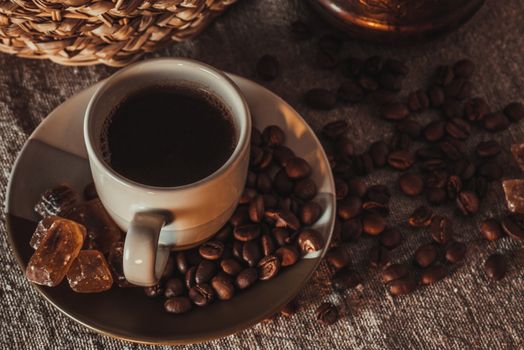 A cup of coffee on textile with coffee beans, dark candy sugar, pots, basket