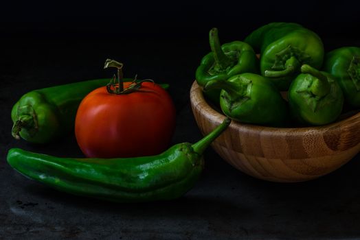 chili pepper and tomato on a dark background. some pepper lie in a wooden bowl. the ingredients for the sauce