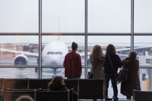People waiting for airplane departure at the airport gates on a rainy day. Bad rainy weather with storms and strong winds causing delays in air traffic.