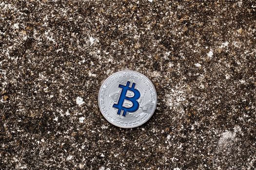 Digital currency physical silver bitcoin coin with blue sign on dark background.