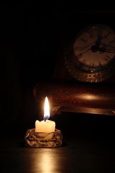 Vintage still life with lighting candle near old clock