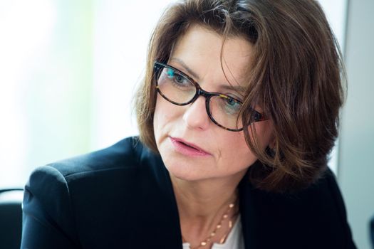 Mature business woman in glasses sitting at meeting table in office