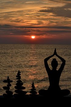 Silhouette of woman in yoga posture and balanced stones at sunrise