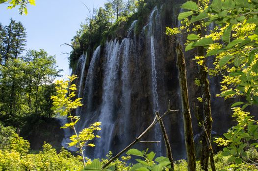 Big waterfall in Plitvice with trees in front and blue sky in background in summer.