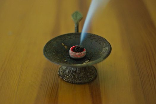 Frankincense burning in bronze cup on brown wooden table