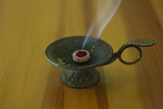 Frankincense burning in bronze cup on brown wooden table