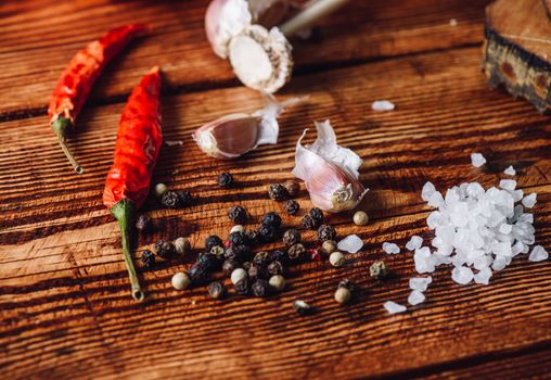 Some condiment lying on wooden table. Red chili pepper with garlic peppercorns and salt.