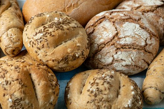 Heap of various bread rolls sprinkled with salt, caraway and sesame. Fresh rustic bread from leavened dough. Assortment of freshly of bakery products