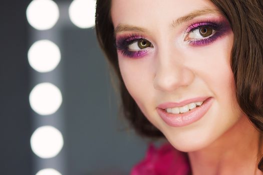 Crop view of attractive female with wavy hair pink lipstick and eye shadows posing at camera on blur background