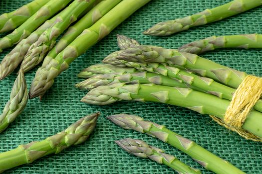 Raw garden asparagus stems. Fresh green spring vegetables on green background. (Asparagus officinalis).