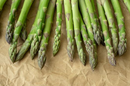 Raw garden asparagus stems. Fresh green spring vegetables on brown wrapping paper. (Asparagus officinalis).