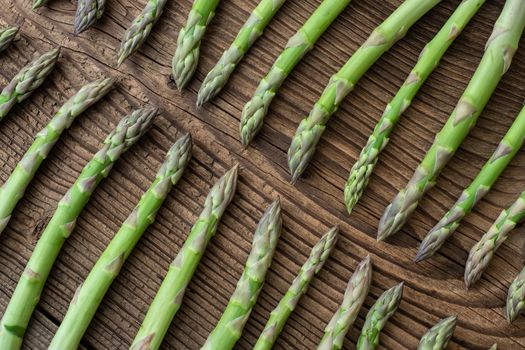 Raw garden asparagus stems. Fresh green spring vegetables on wooden background. (Asparagus officinalis).