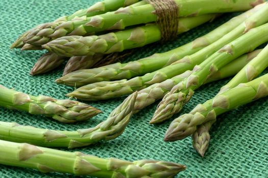 Raw garden asparagus stems. Fresh green spring vegetables on green background. (Asparagus officinalis).