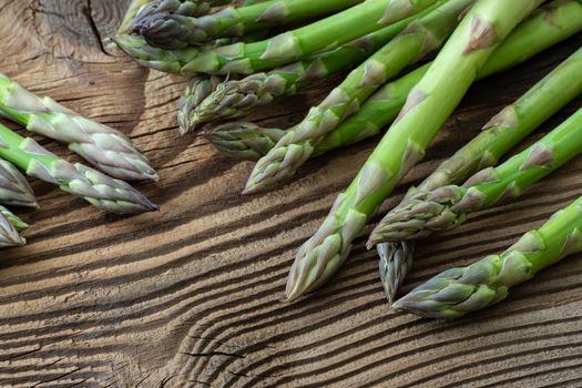 Raw garden asparagus stems. Fresh green spring vegetables on wooden background. (Asparagus officinalis).