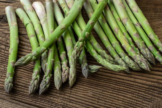 Raw garden asparagus stems. Fresh green spring vegetables on wooden background. (Asparagus officinalis).