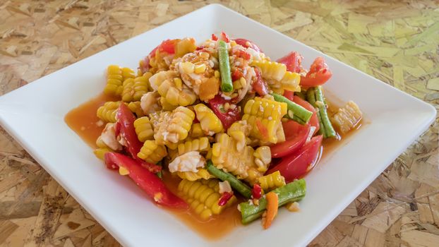 spicy sweet corn salad with salted egg in white plate over wooden background  ,Thai style food