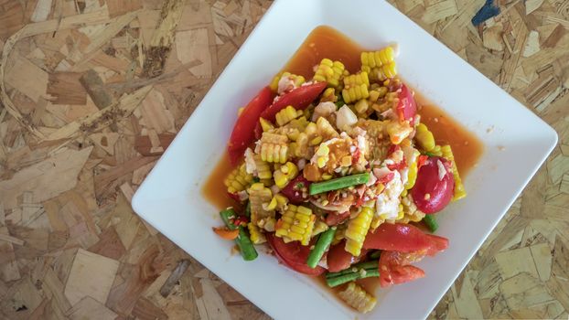 spicy sweet corn salad with salted egg in white plate over wooden background  ,Thai style food