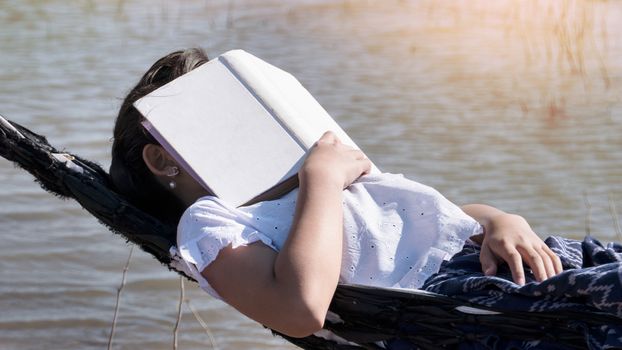 Close up of young beautiful girl sleeping in a hammock and holding a book with her hands