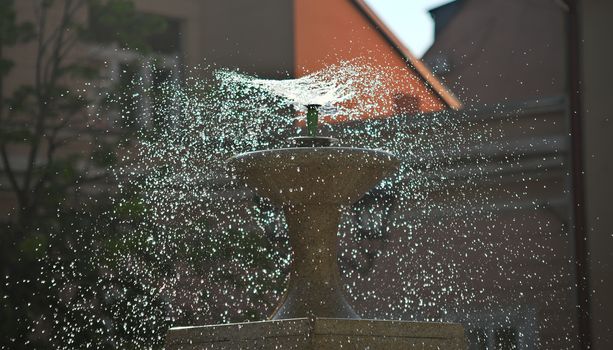 droplets dispersing from a fountain and buildings in background