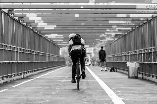 Man riding his bike in the cycling lane on Williamsburg Bridge, Brooklyn, New York City, USA. Black and white image.