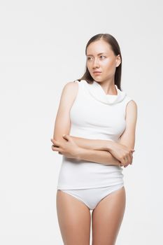 Beautiful young woman in panties and turtleneck top keeping arms folded and looking away while standing on white background