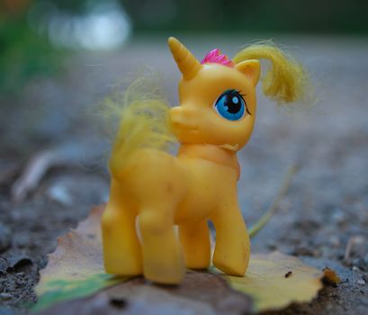 Yellow toy unicorn standing on leaf at forest road