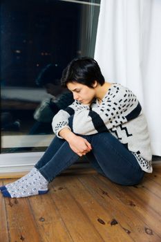 Sad woman sitting on the floor in corner of room, portrait of a sad teenage girl looking thoughtful about troubles. Lonely Depressed woman.