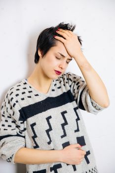 Portrait of young upset and stressed woman standing near the wall with headache and lot of problems.