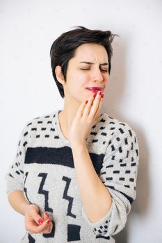 Portrait of young upset and stressed woman standing near the wall with toothache and lot of problems.