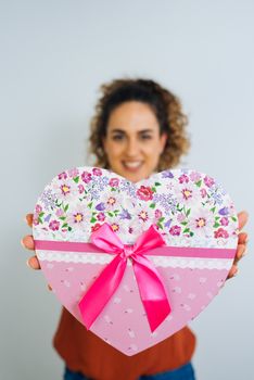 Attractive Curly Long Haired Woman Is Holding A Heart Shaped Box With Ribbon Isolated On White Background