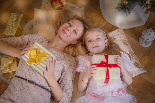 Mother and daughter lying with gifts under Christmas tree, top view