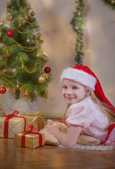 Cute girl in Santa hat dreaming under Christmas tree