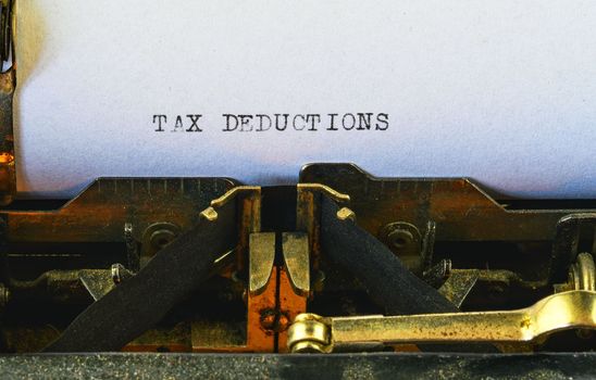 Closeup on vintage typewriter. Front focus on letters making TAX DEDUCTIONS text. Business concept image with retro office tool.