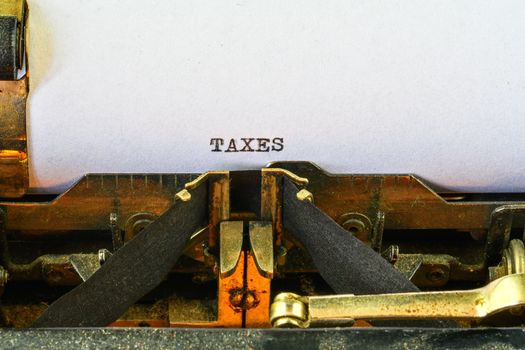 Closeup on vintage typewriter. Front focus on letters making TAXES text. Business concept image with retro office tool.