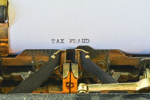 Closeup on vintage typewriter. Front focus on letters making TAX FRAUD text. Business concept image with retro office tool.