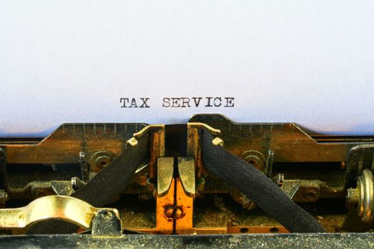 Closeup on vintage typewriter. Front focus on letters making TAX SERVICE text. Business concept image with retro office tool.