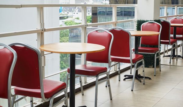 Empty of red chairs and round wooden tables outside cafeteria in high building.