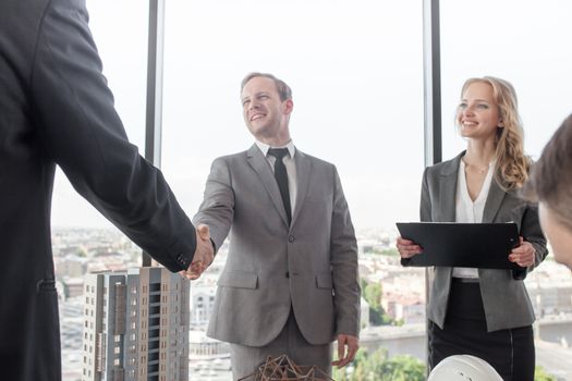 Business meeting of architects and investors shaking hands finishing deal, model of modern multi storey residential building house on table