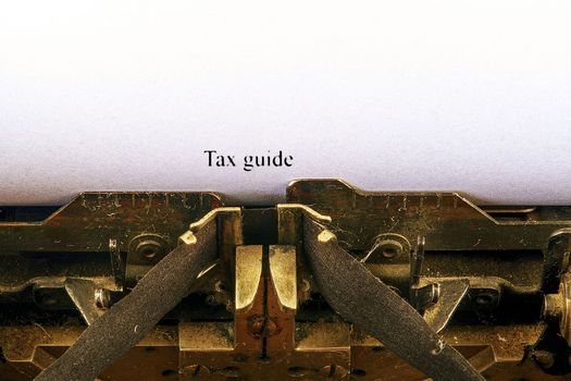 Closeup on vintage typewriter. Front focus on letters making TAX GUIDE text. Business concept image with retro office tool.