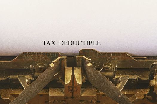 Closeup on vintage typewriter. Front focus on letters making TAX DEDUCTIBLE  text. Business concept image with retro office tool.