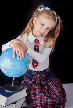 Schoolgirl with globe sitting on black background, education and school concept