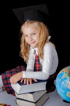Schoolgirl with hat and globe sitting on black background, education and school concept