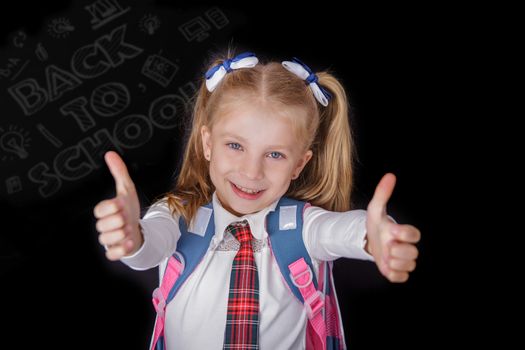 Schoolgirl showing thumbs up sign using both hands at chalkboard with back to school words