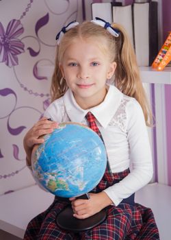 Cute schoolgirl with globe sitting on table, school and education concept