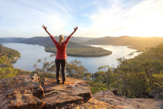 A woman enjoys the warm golden sunlight in the afternoon and cliff top views across the mountains and river