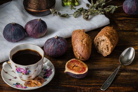 Cup of coffee with fresh bread and some ripe figs on wooden surface